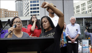 Marissa Johnson, left, speaks as Mara Jacqueline Willaford holds her fist overhead and Democratic presidential candidate Sen. Bernie Sanders, I-Vt., stands nearby as the two women take over the microphone at a rally Saturday, Aug. 8, 2015, in downtown Seattle. The women, co-founders of the Seattle chapter of Black Lives Matter, took over the microphone and refused to relinquish it. Sanders eventually left the stage without speaking and instead waded into the crowd to greet supporters. (AP Photo/Elaine Thompson)