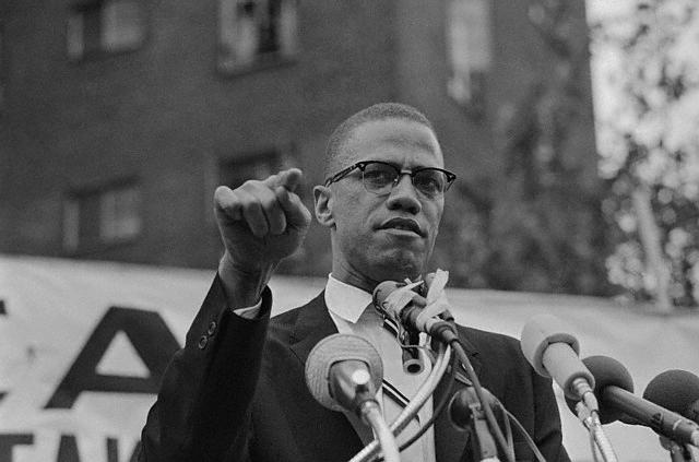 Malcolm X Shown with a Clenched Fist Speaking at a Rally