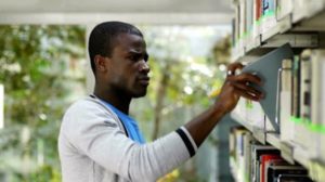 stock-footage-african-american-male-college-student-taking-book-from-shelf-in-library-and-looking-at-camera