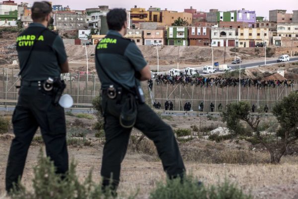 Spanish Guardia Civil watch as would be immigrants from Africa sit atop a wire-meche fence after scrambling over two other border barriers on Spain's tiny north African territory of Melilla on August 13, 2014.  Some 600 people tried to scale the triple-layer six-metre-high (20-foot) razor-wire barrier that separates Morocco from Melilla in a pre-dawn assault today, said Irene Flores, spokeswoman for the Spanish government in Melilla. More than 60 of them had perched on the top of the border fence, she told AFP. AFP PHOTO / JOSE COLONJOSE COLON/AFP/Getty Images ** OUTS - ELSENT, FPG - OUTS * NM, PH, VA if sourced by CT, LA or MoD **