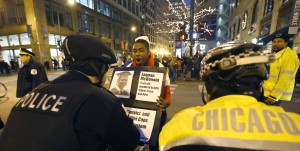 Dontreal Widow holds up a poster with the photo of  17 year-old Laquan McDonald and taunts Chicago police officers Wednesday, Nov. 25, 2015, one day after murder charges were brought against police officer Jason Van Dyke in the killing of McDonald, in Chicago. (AP Photo/Charles Rex Arbogast)