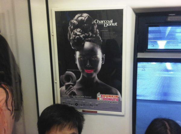 An advertisement poster of a smiling woman with bright pink lips in blackface makeup holding a doughnut is seen on a Skytrain, a commuter train in Bangkok, Thailand, Friday, Aug. 30, 2013. A leading human rights group has called on Dunkin' Donuts to withdraw the "bizarre and racist" advertisement for chocolate doughnuts in Thailand. The Dunkin' Donuts franchise in Thailand launched a campaign earlier this month for its new "Charcoal Donut" featuring the image, which is reminiscent of 19th and early 20th century American stereotypes for black people that are now considered offensive symbols of a racist era. (AP Photo/Grant Peck)