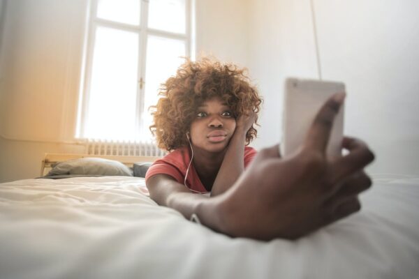 Woman on her bed scrolling through cell phone (Photo by Andrea Piacquadio via Pexels)